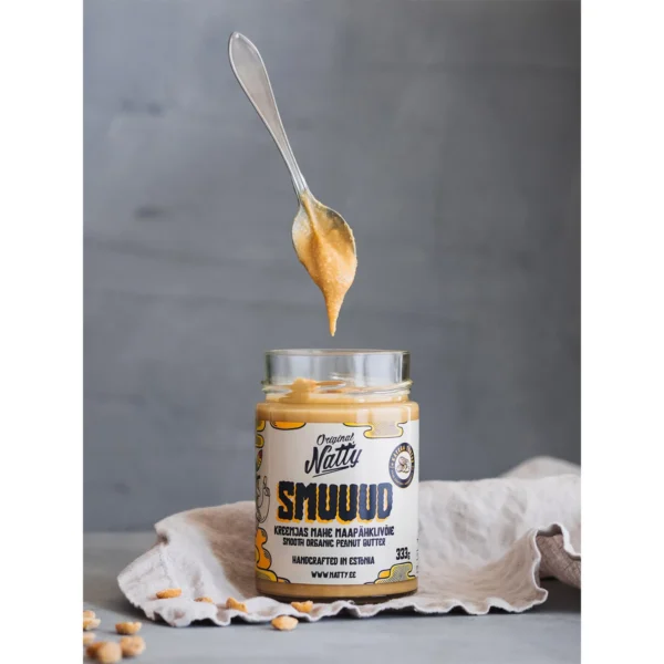 Spoonful of smooth peanut butter above an open Natty Smuuud jar