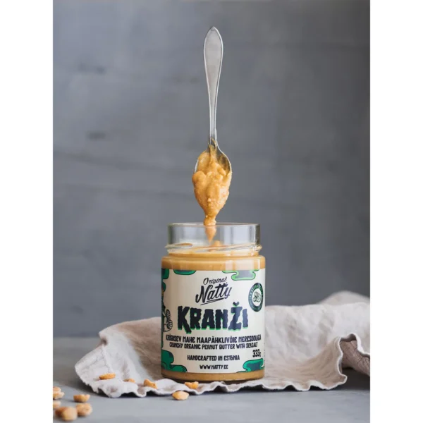 Spoonful of crunchy peanut butter above an open Natty Kranži jar