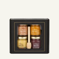 Gift set of four 50 g honey jars with a wooden honey dipper in a black window box on a warm light background.